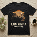 Photographic mugshot of a crested gecko braced wide-eyed above the hook I Jump At Faces, no warning. — shown on a Black tee.