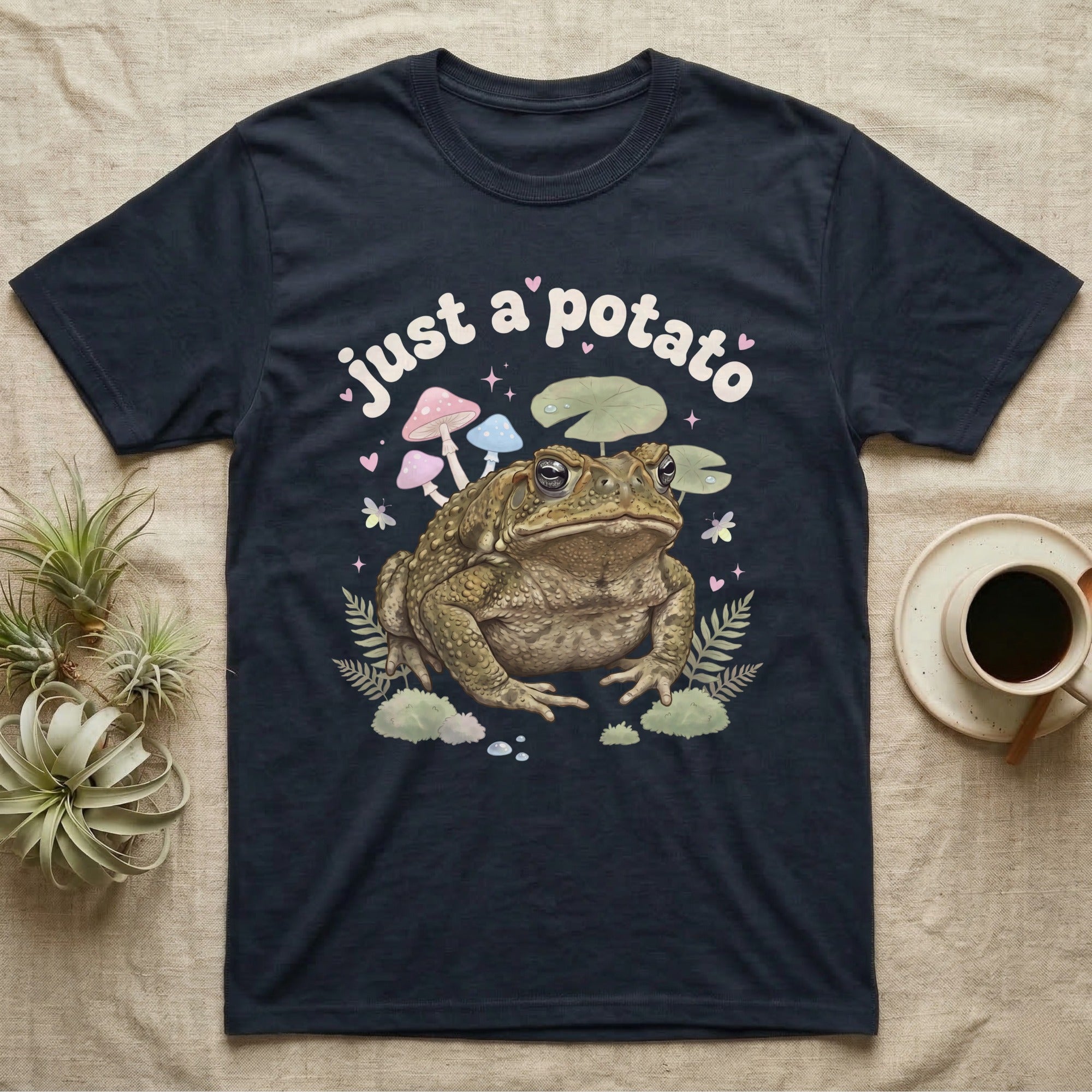 Cane Toad Baby T-Shirt in Navy — Warty cane toad among pastel toadstools and lily pads under puffy cream bubble text "just a potato".