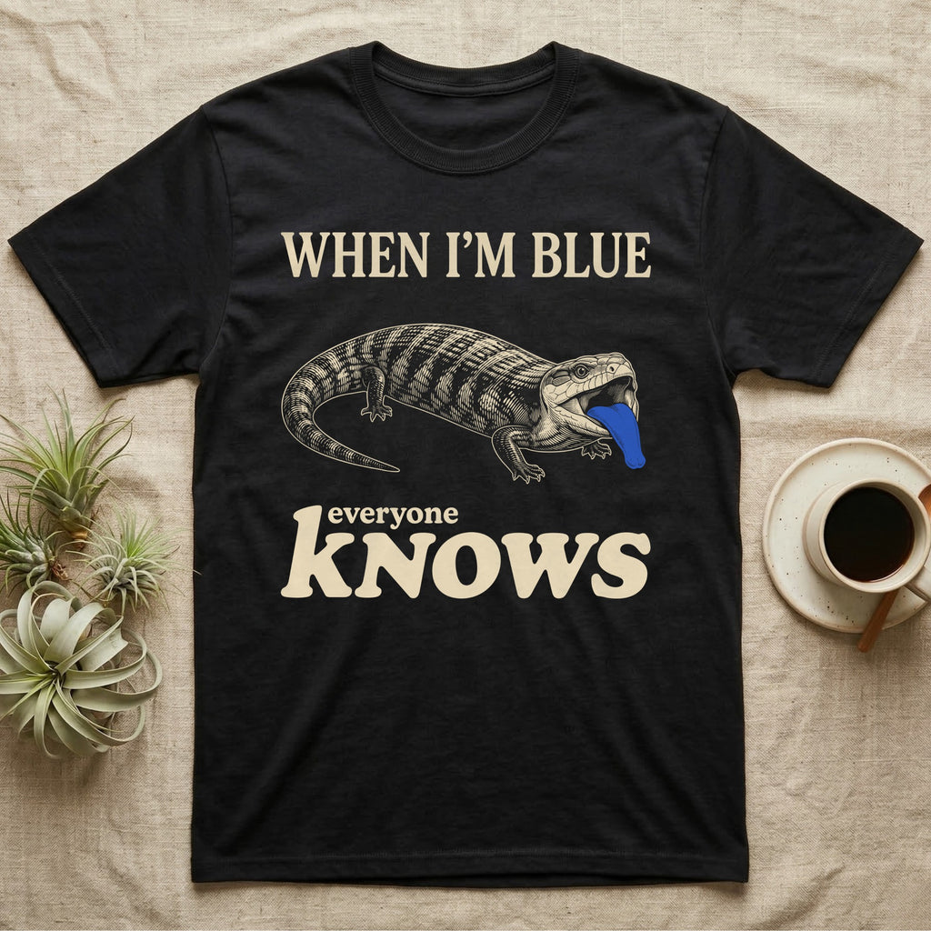 Blue-Tongue Skink Mood T-Shirt in Black — Cream engraved blue-tongued skink on black flashing a cobalt blue tongue under the words WHEN I'M BLUE everyone KNOWS