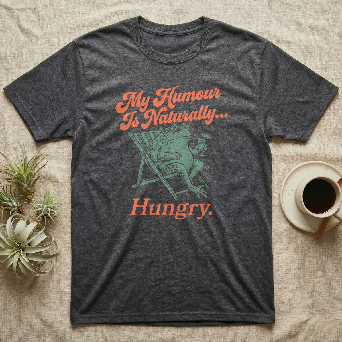 African Bullfrog Sun Lounger T-Shirt in Dark Heather — Illustrated African bullfrog reclining in a beach chair with sunglasses and a cocktail, retro coral script reading My Humour Is Naturally Hungry.