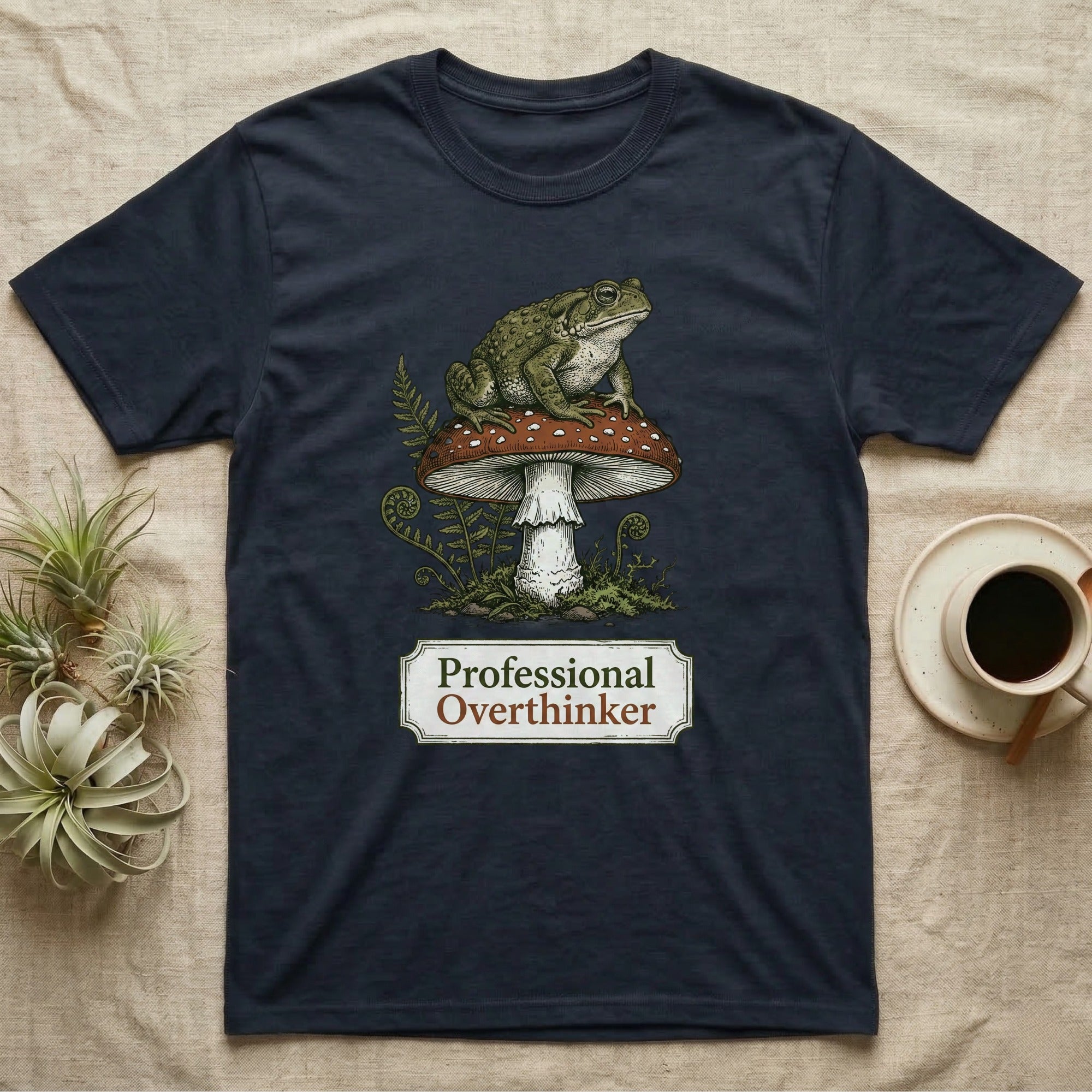 Dark t-shirt with a frog on a mushroom, saying "Professional Overthinker".