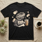 Cold Brew Bearded Dragon T-Shirt in Black — Flat near-photoreal illustration of a bearded dragon in tiny sunglasses holding a cold brew with warm bokeh.