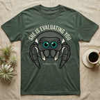 Phidippus Regius Jumping Spider Tee in Military Green — Vector-bold front-facing regal jumping spider portrait with electric-teal anterior-median eyes on a cream-and-charcoal body.