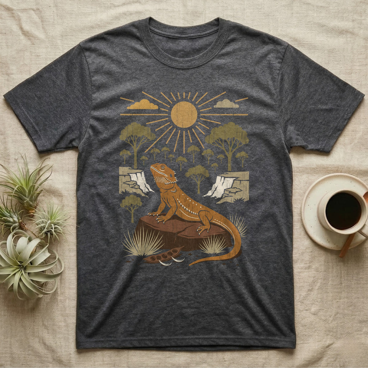 Bearded Dragon Home Range T-Shirt in Dark Heather — Woodcut-style illustration of a bearded dragon basking on a boulder under a full sun with arid scrub trees and escarpments behind, no on-shirt text.