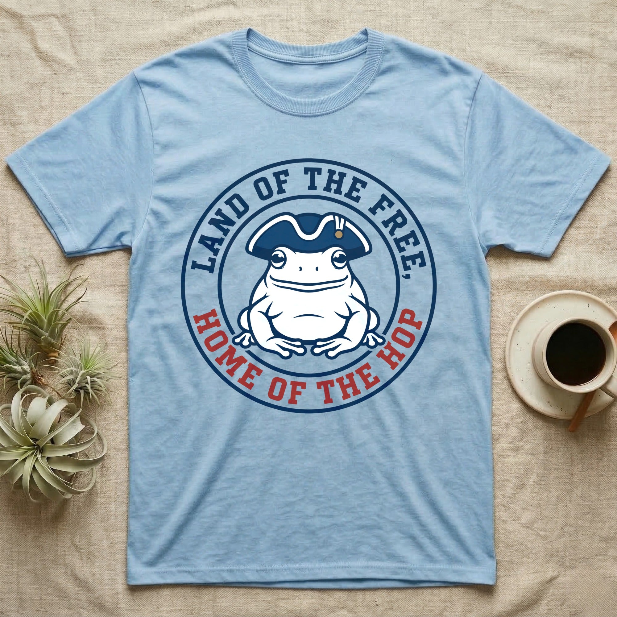 American Toad Emblem T-Shirt in Light Blue — Round emblem of a white American toad silhouette in a tricorn hat with text Land of the Free, Home of the Hop.