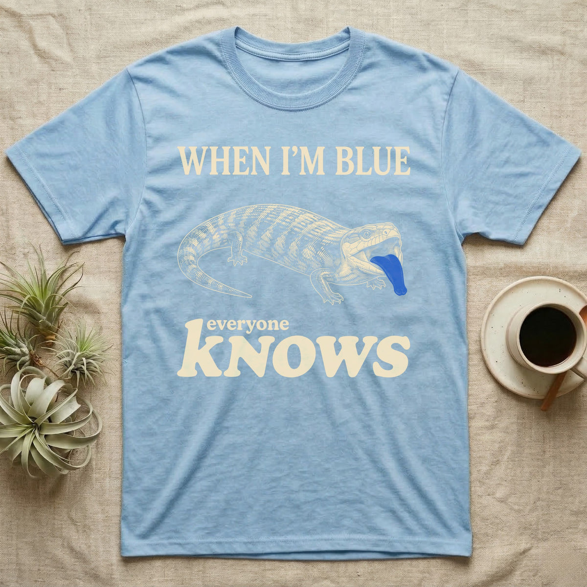 Blue-Tongue Skink Mood T-Shirt — Cream engraved blue-tongued skink on black flashing a cobalt blue tongue under the words WHEN I'M BLUE everyone KNOWS