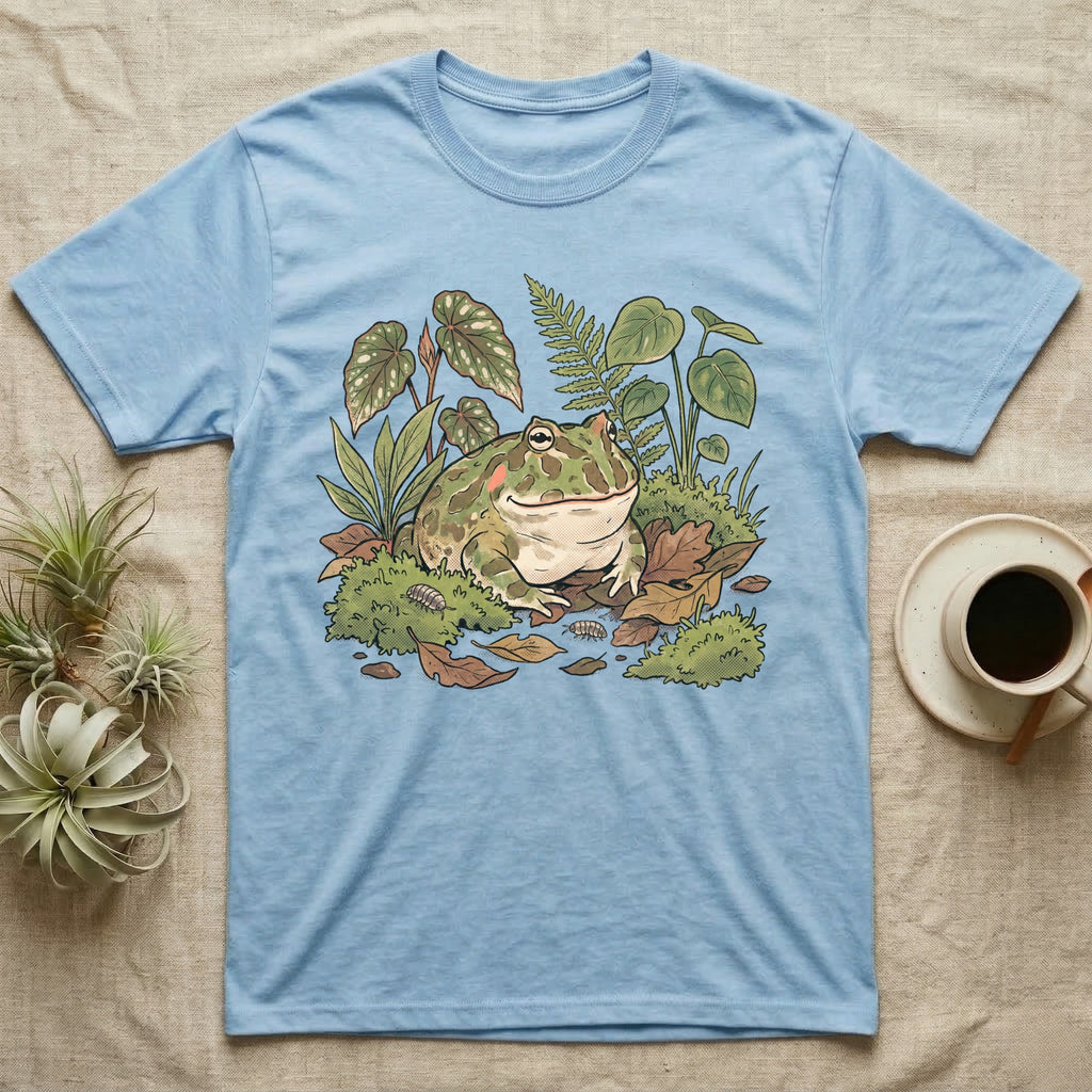 Bioactive Pacman Frog T-Shirt in Light Blue — Warm botanical illustration of a content pacman frog half-buried in a lush bioactive habitat of moss and leaf litter.