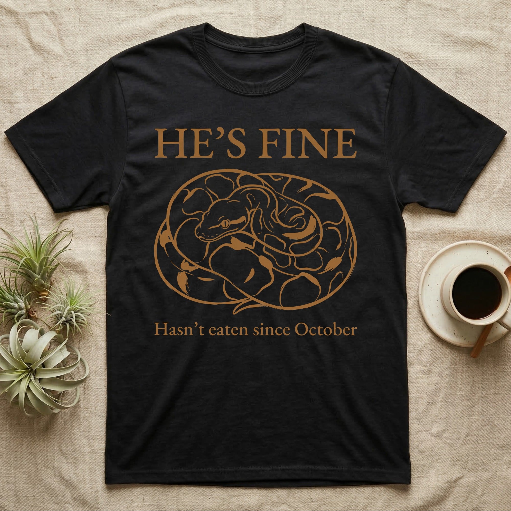 Ball Python He's Fine T-Shirt in Black — One-ink linocut illustration of a ball python coiled into a tight defensive ball with "He's Fine" deadpan lettering above and below.