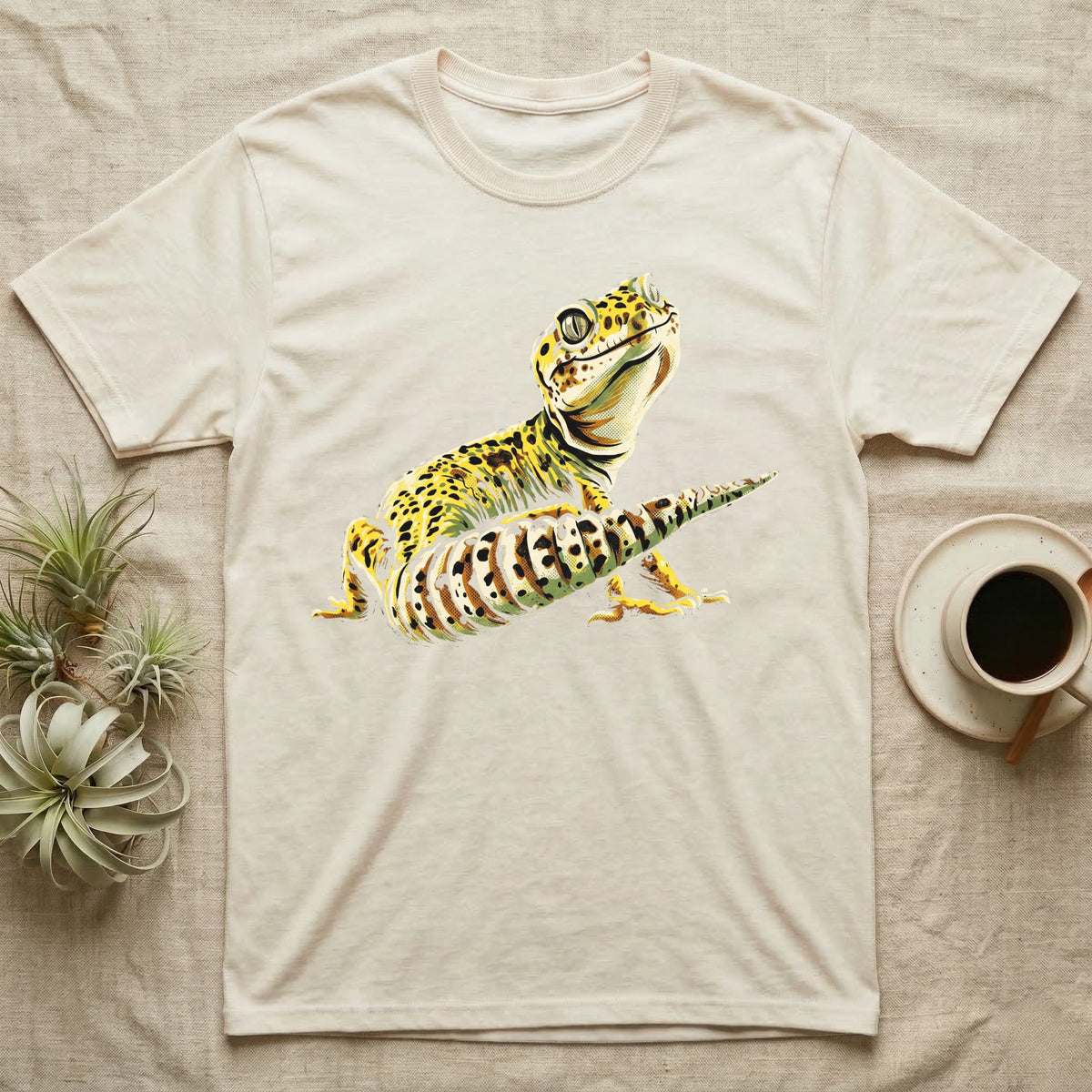 Illustration of a smiling leopard gecko with a plump curled spotted tail, bold vintage-comic ink outlines and halftone shading, graphic-only, no text. — shown on a Natural tee.
