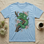 Green snake coiled on a tree branch with pink blossoms on a light blue t-shirt.