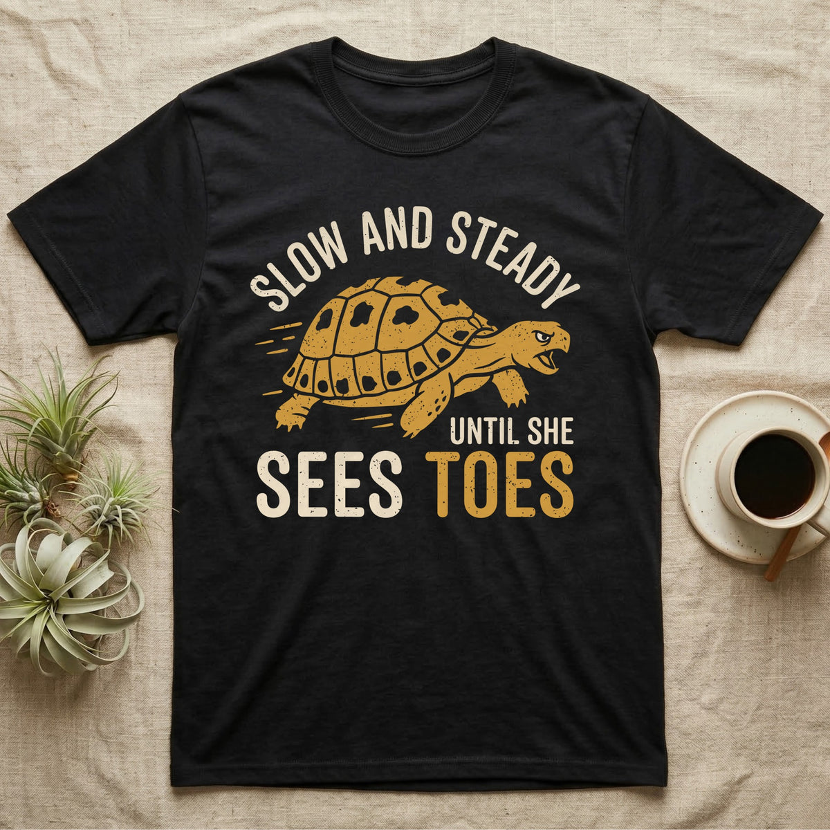 Hermann's Tortoise Toes T-Shirt in Black — Golden ochre Hermann's tortoise charging to the right under arched cream words Slow And Steady, with Until She Sees Toes below