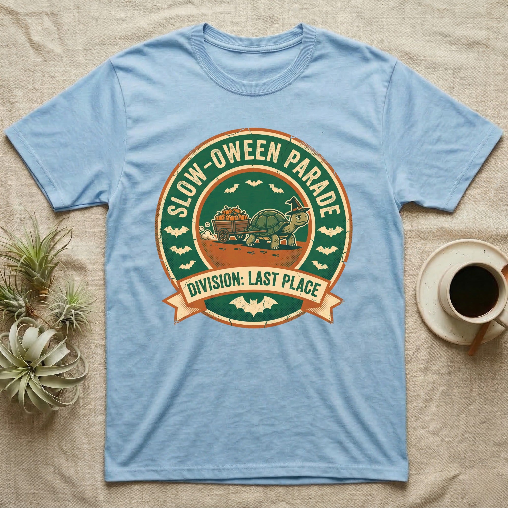 Tortoise Slow-oween Parade T-Shirt in Light Blue — Distressed badge of a witch-hatted tortoise pulling a pumpkin wagon, "Slow-oween Parade, Division Last Place."