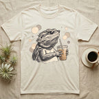 Cold Brew Bearded Dragon T-Shirt in Natural — Flat near-photoreal illustration of a bearded dragon in tiny sunglasses holding a cold brew with warm bokeh.