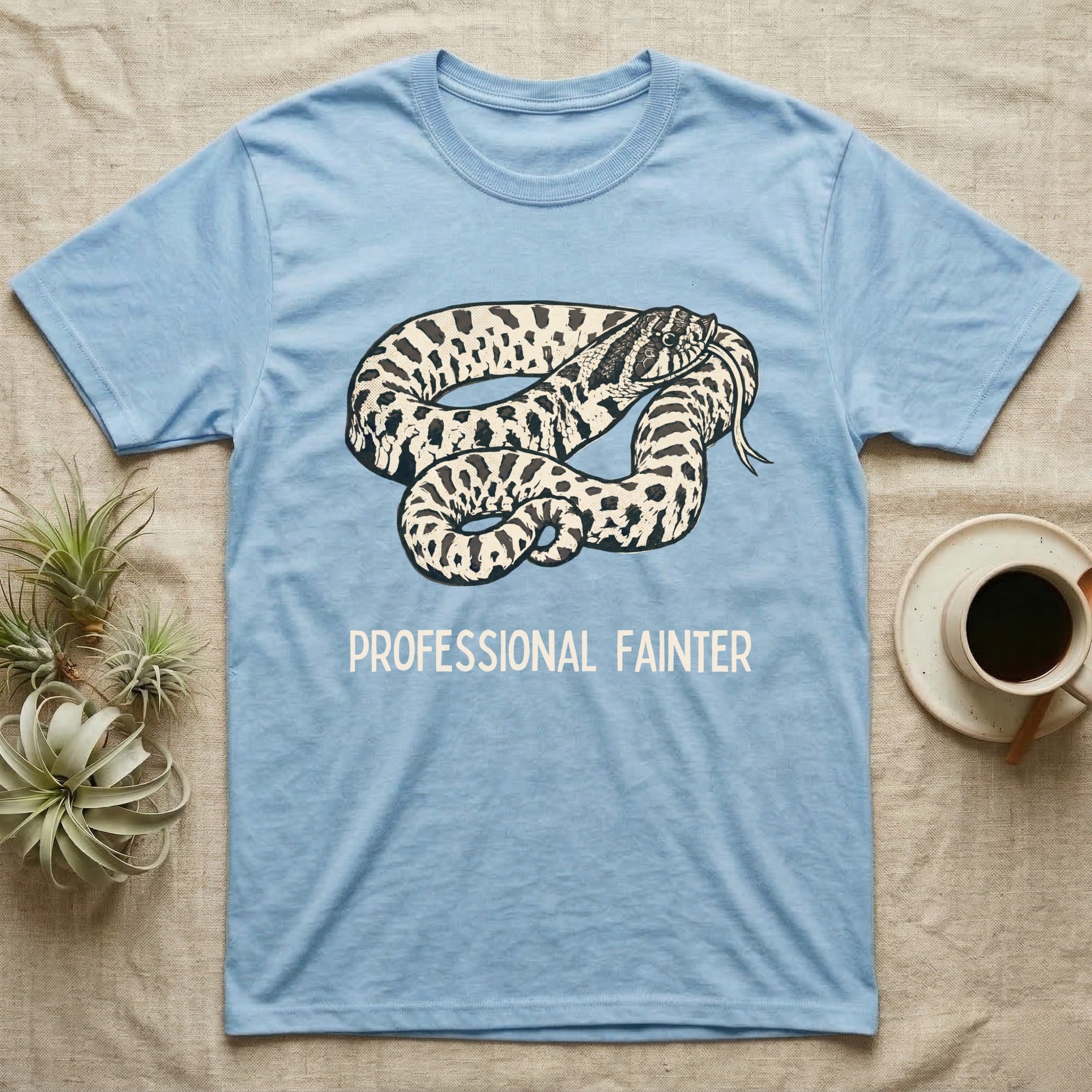 Hognose Professional Fainter T-Shirt in Light Blue — Linocut block-print of a western hognose snake flopped belly-up in a death-feign with professional fainter caption.