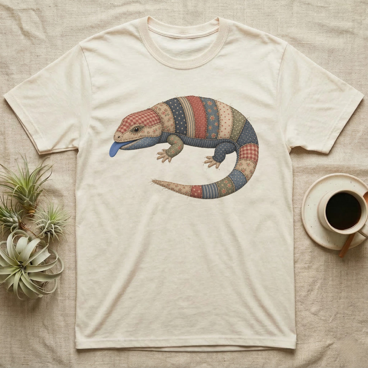 Cream t-shirt with a quilt-patterned lizard graphic and blue tongue.