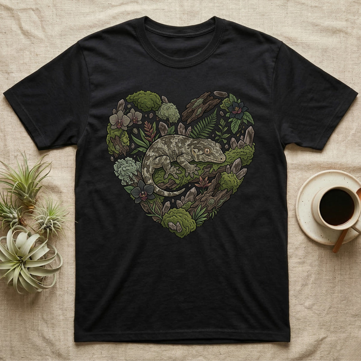 Black t-shirt with a heart-shaped design of a gecko surrounded by plants and moss.