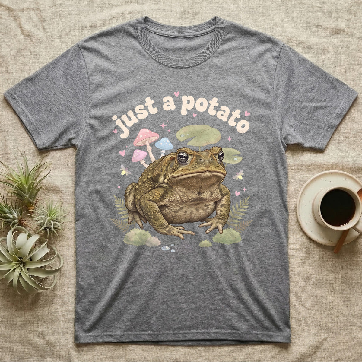 Cane Toad Baby T-Shirt in Sport Grey — Warty cane toad among pastel toadstools and lily pads under puffy cream bubble text "just a potato".