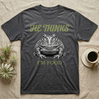 Pacman Frog He Thinks I'm Food T-Shirt in Dark Heather — Engraved white-line illustration of a pacman frog staring straight ahead below retro script lettering reading HE THINKS.