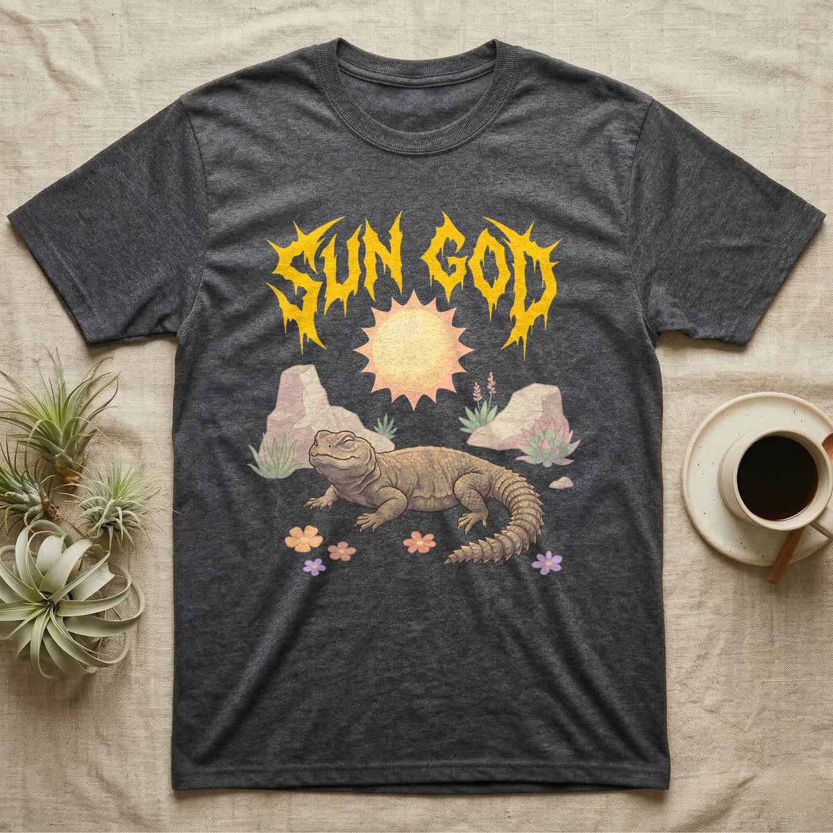 Moroccan Uromastyx Feral T-Shirt in Dark Heather — Moroccan uromastyx basking under a big sun with a jagged solar-gold metal "SUN GOD" wordmark and pastel desert scene.