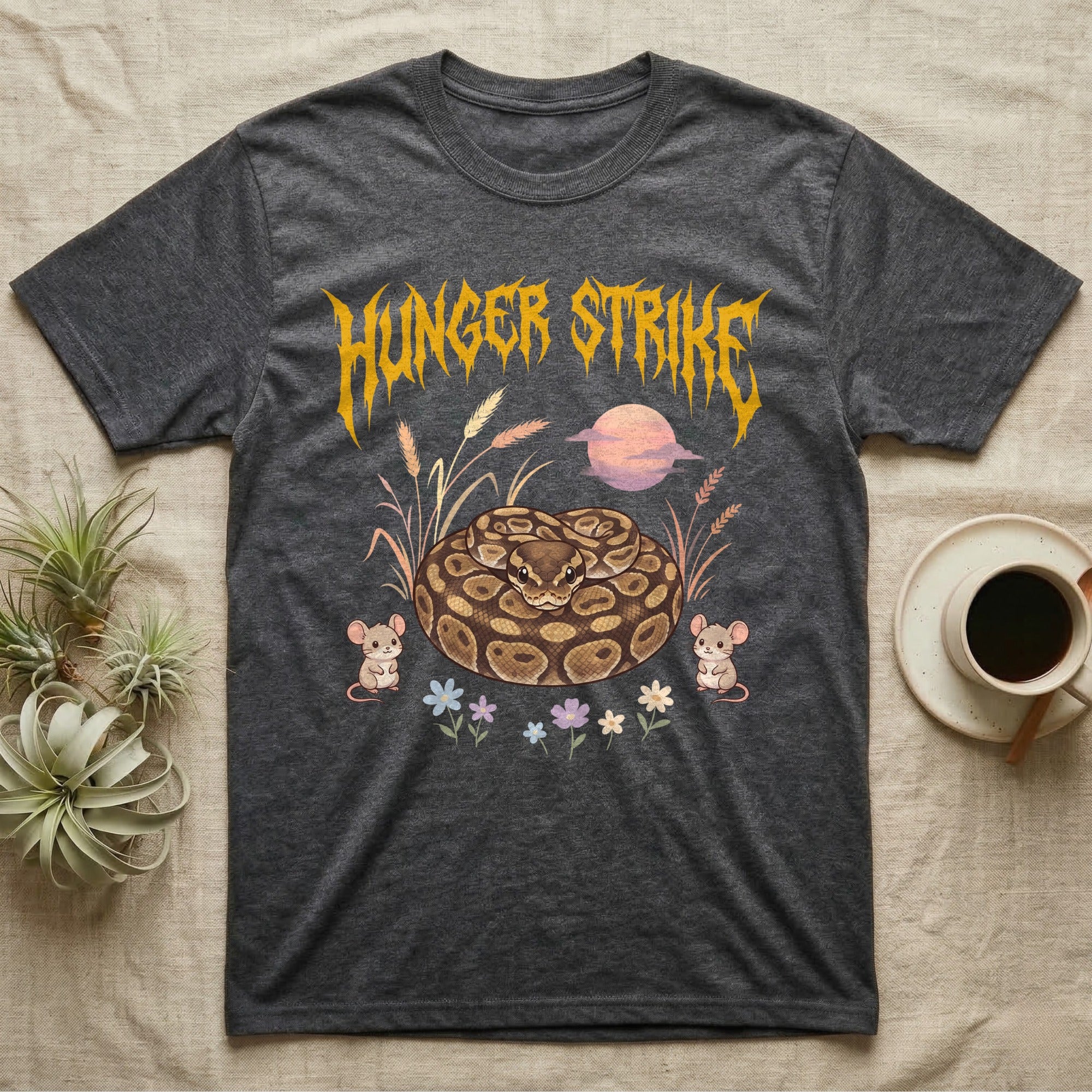 Ball Python Feral T-Shirt in Dark Heather — Ball python coiled in a loaf in a pastel savanna scene under a spiky honey-gold metal wordmark reading HUNGER STRIKE.