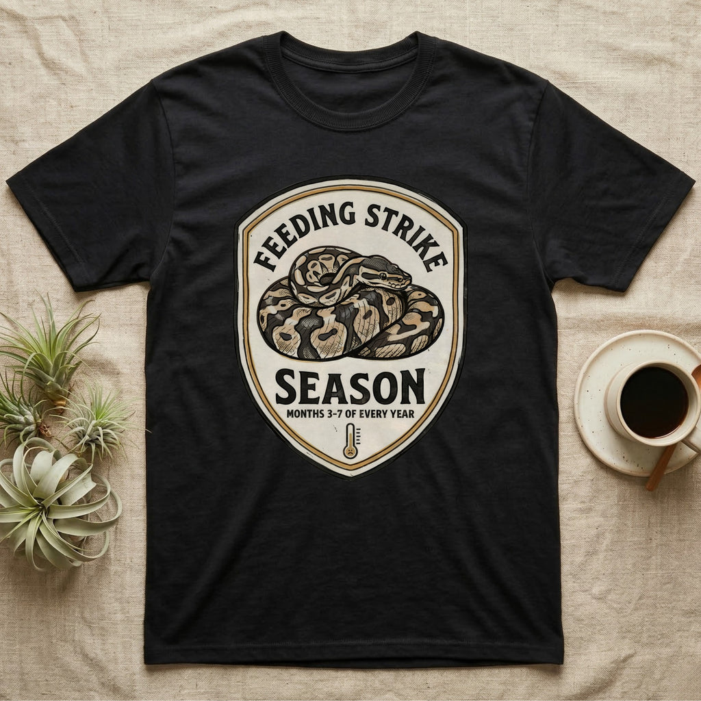 Ball Python Feeding Strike T-Shirt in Black — Vintage-ink badge of a coiled ball python with carved type "Feeding Strike Season" and fine print "Months 3-7 Of Every Year."