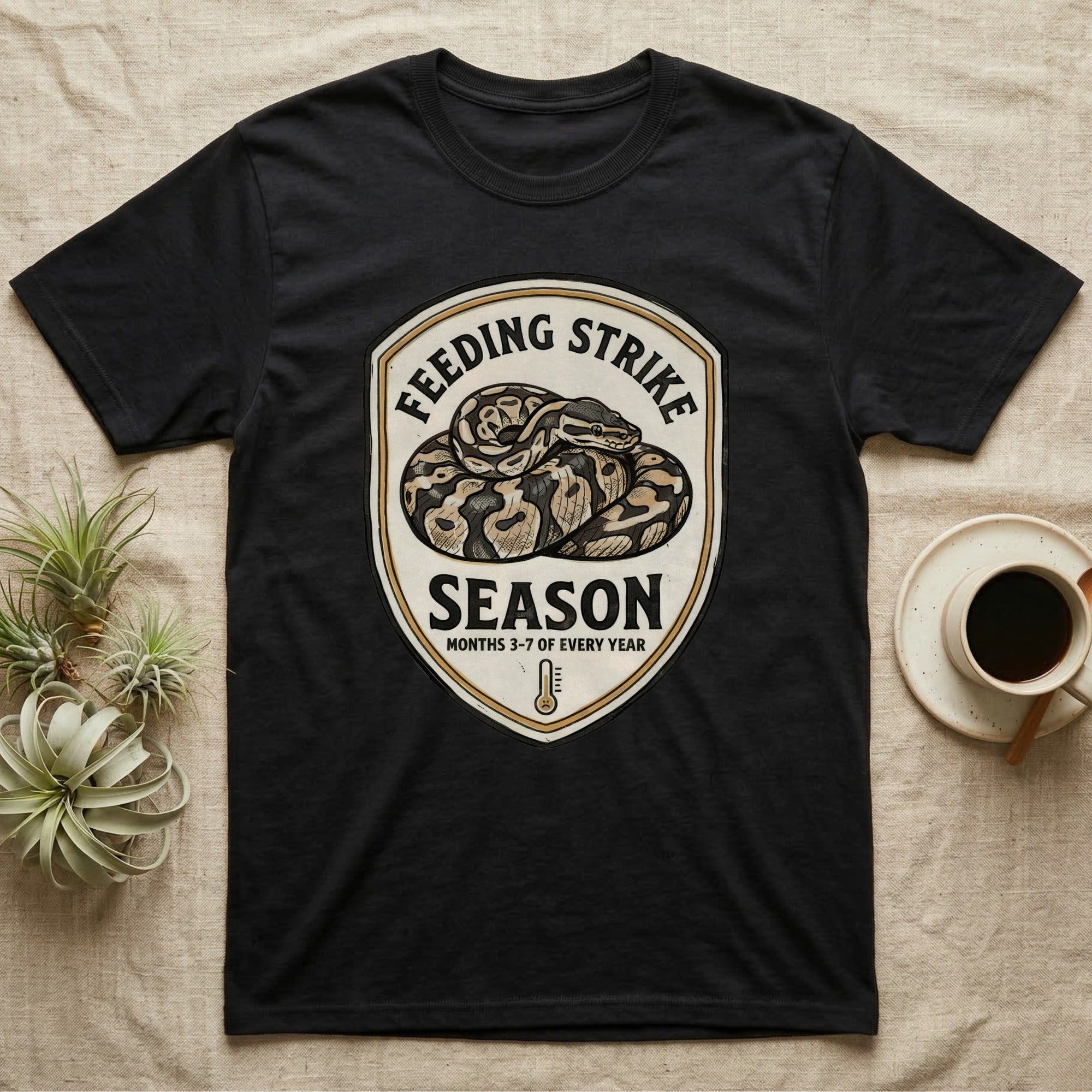 Ball Python Feeding Strike T-Shirt in Black — Vintage-ink badge of a coiled ball python with carved type "Feeding Strike Season" and fine print "Months 3-7 Of Every Year."