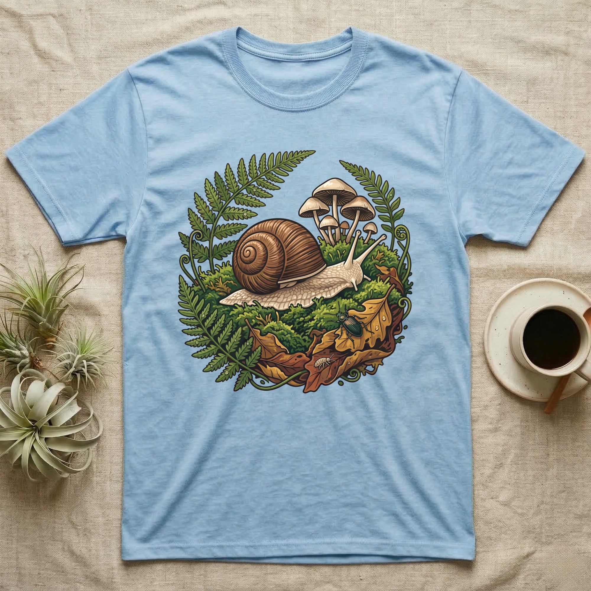 Garden Snail Moss Terrarium T-Shirt in Light Blue — Garden snail crossing moss inside a circular forest vignette of ferns, mushrooms, oak leaves and a beetle.