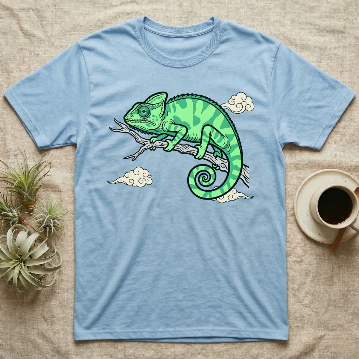 Light blue t-shirt with a green chameleon on a branch and clouds design.