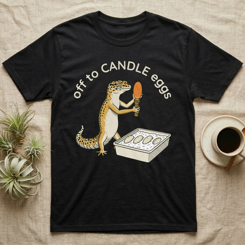 Leopard Gecko Candling T-Shirt in Black — Leopard gecko holding a torch under a glowing orange egg beside a tub of eggs, under the words off to CANDLE eggs