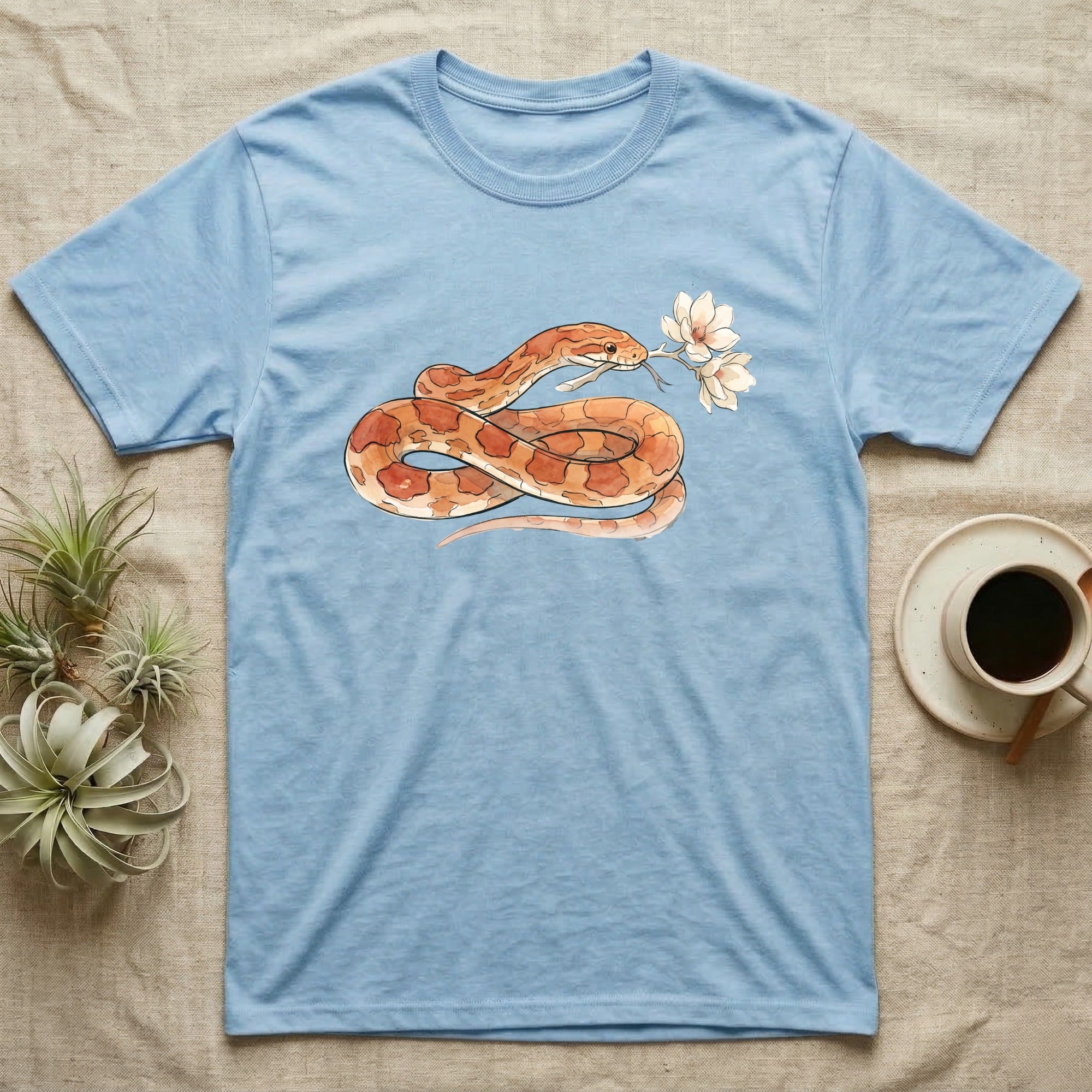 Corn Snake Blossom T-Shirt in Light Blue — Watercolor illustration of an orange-and-cream corn snake holding a magnolia blossom sprig, on a dark grey t-shirt.