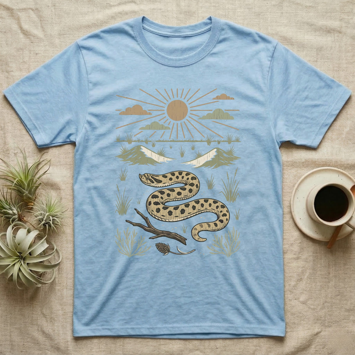 Western Hognose Home Range T-Shirt in Light Blue — Woodcut-style illustration of a western hognose snake nosing through sand with dunes and sagebrush behind, no on-shirt text.