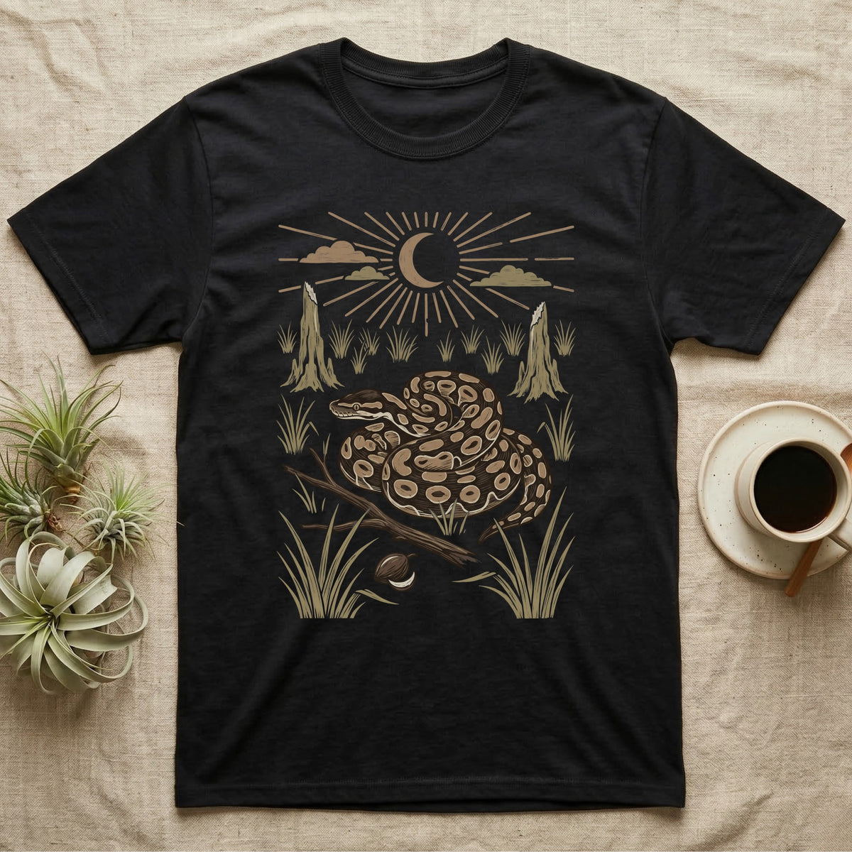 Ball Python Home Range T-Shirt in Black — Woodcut-style illustration of a ball python coiled on dry savanna ground with grass tufts and termite mounds behind, no on-shirt text.