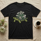 Black t-shirt with a green turtle carrying a mountain and clouds on its shell.