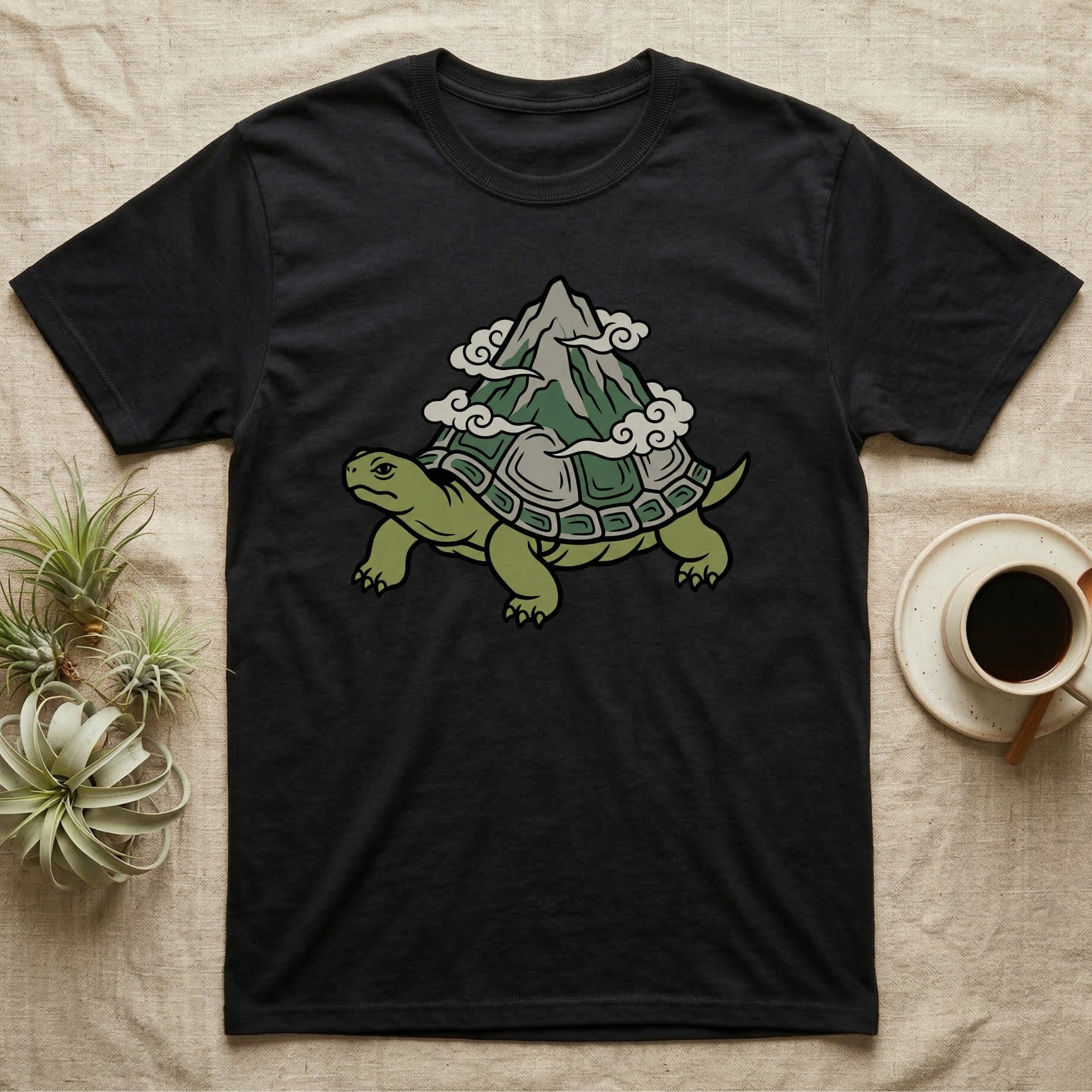 Black t-shirt with a green turtle carrying a mountain and clouds on its shell.
