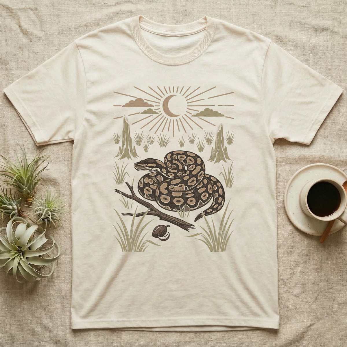 Ball Python Home Range T-Shirt in Natural — Woodcut-style illustration of a ball python coiled on dry savanna ground with grass tufts and termite mounds behind, no on-shirt text.