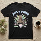 Asian Water Monitor Baby T-Shirt in Black — Asian water monitor with tongue out among pastel reeds and lotus under puffy blue bubble text "just a puppy".