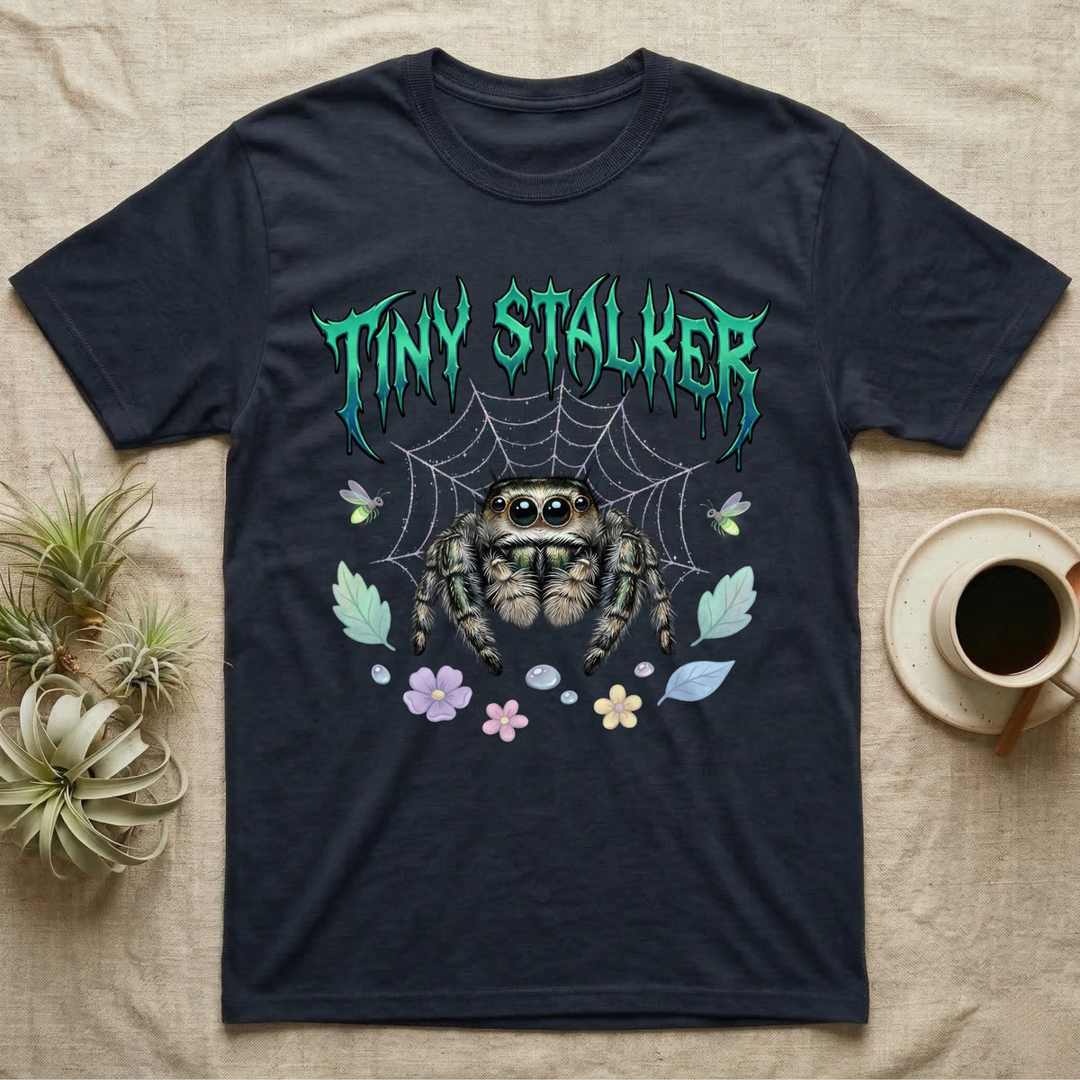 Regal Jumping Spider Feral T-Shirt in Navy — Fuzzy jumping spider with huge eyes in a pastel garden under a spiky iridescent-teal metal wordmark reading TINY STALKER.