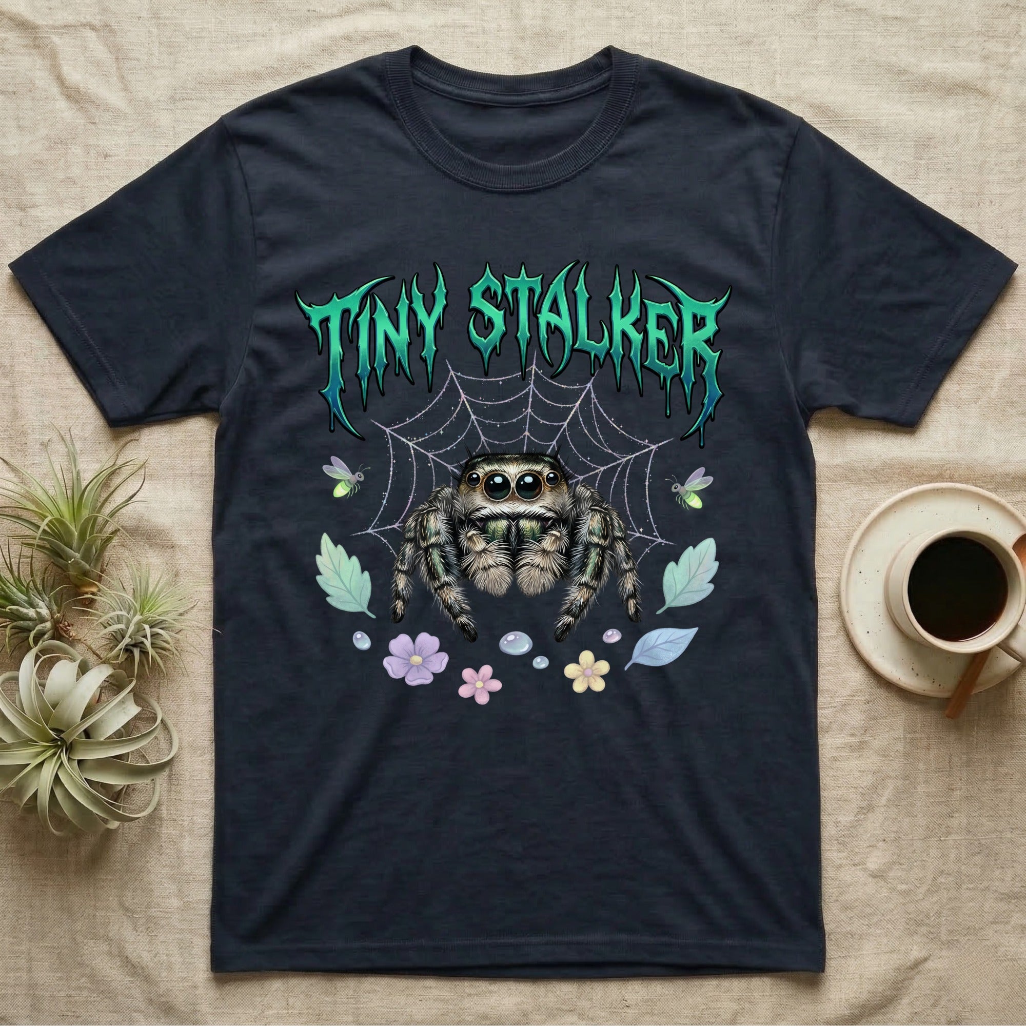 Regal Jumping Spider Feral T-Shirt in Navy — Fuzzy jumping spider with huge eyes in a pastel garden under a spiky iridescent-teal metal wordmark reading TINY STALKER.
