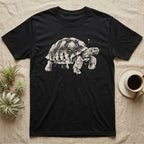 Sulcata Bleach Spatter T-Shirt in Black — Sulcata tortoise marching to the right, head up and one scaly front leg mid-step, formed from pale bleach spatter on black.