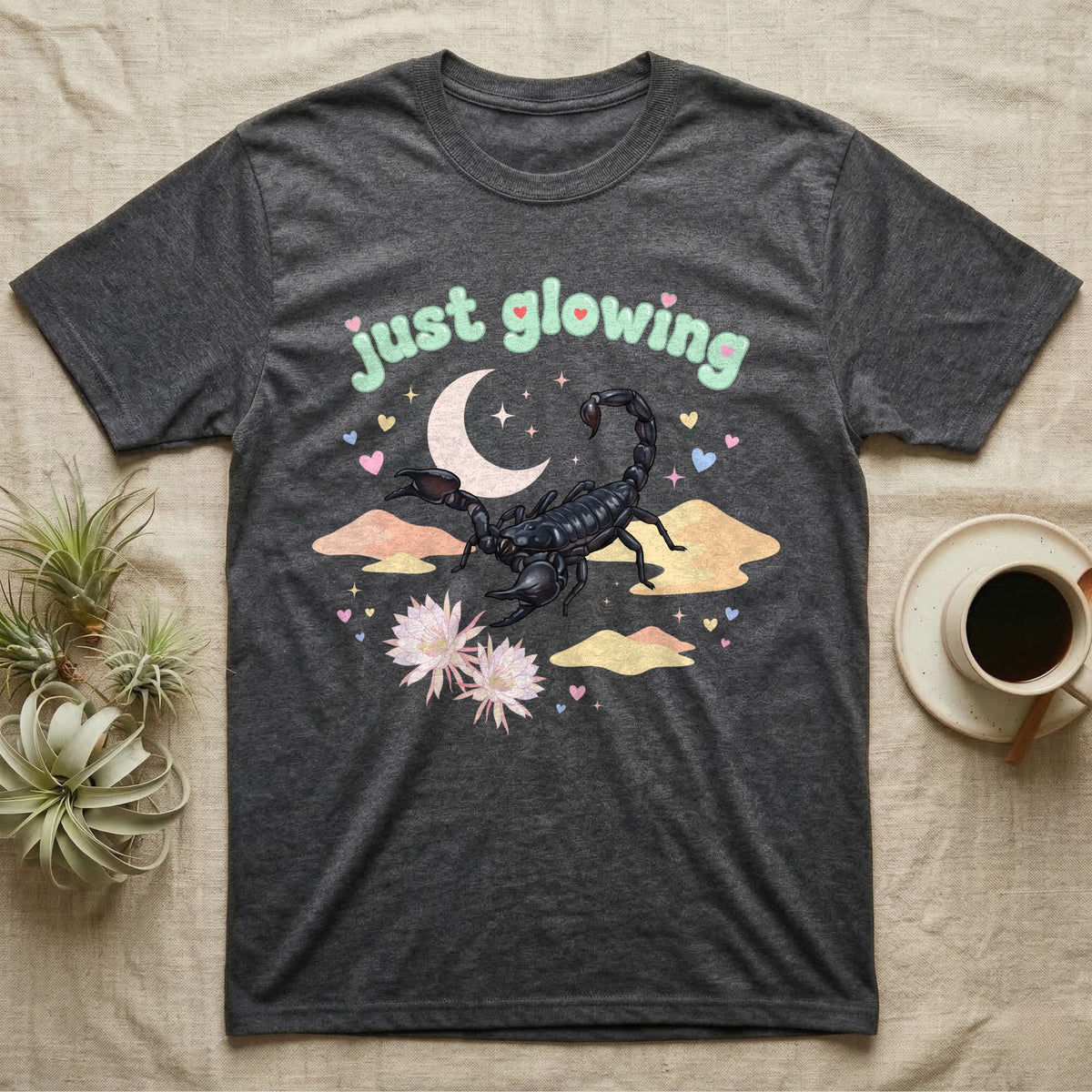 Emperor Scorpion Baby T-Shirt in Dark Heather — Black emperor scorpion, pincers raised, under a pastel moon and stars with puffy mint bubble text "just glowing".