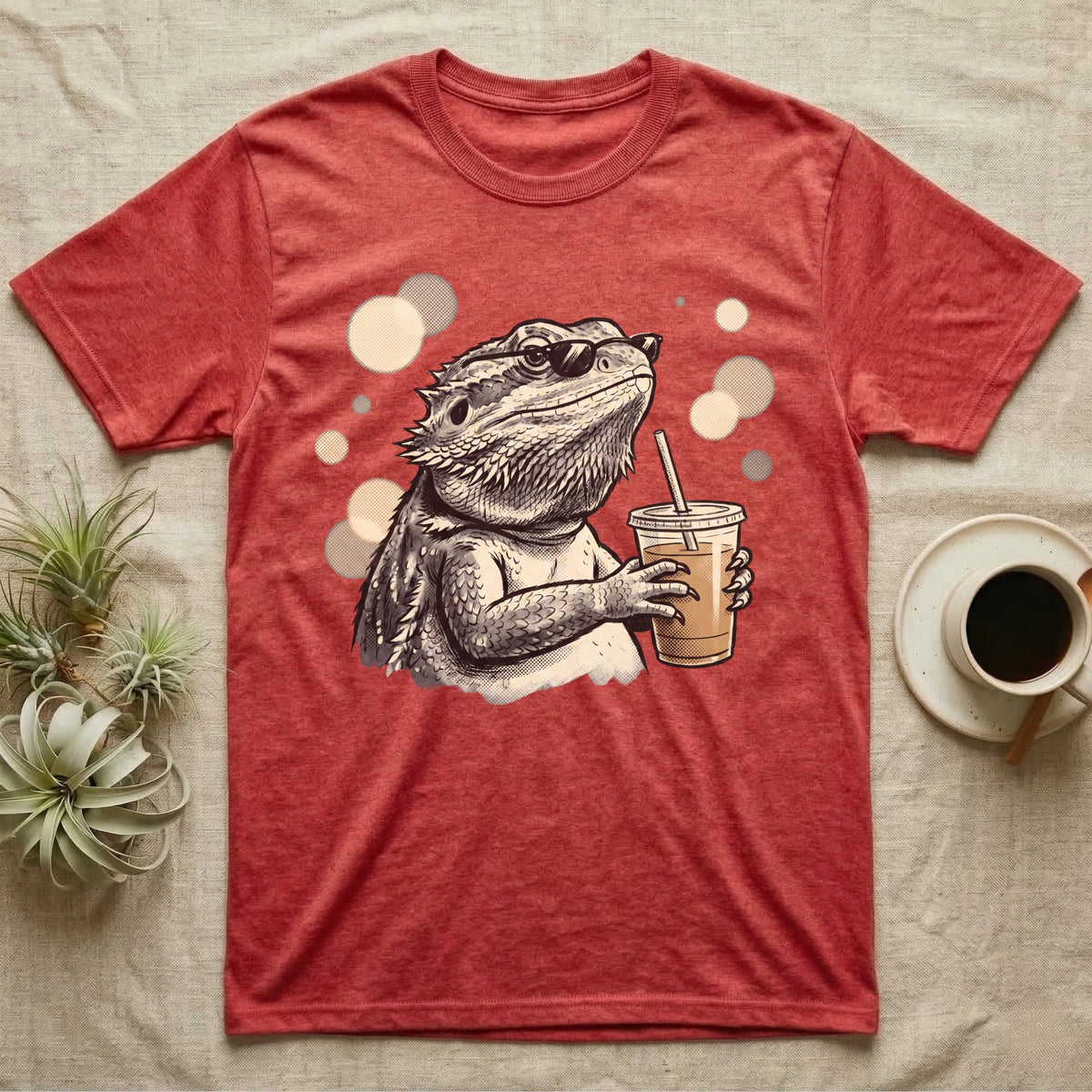 Cold Brew Bearded Dragon T-Shirt in Heather Red — Flat near-photoreal illustration of a bearded dragon in tiny sunglasses holding a cold brew with warm bokeh.
