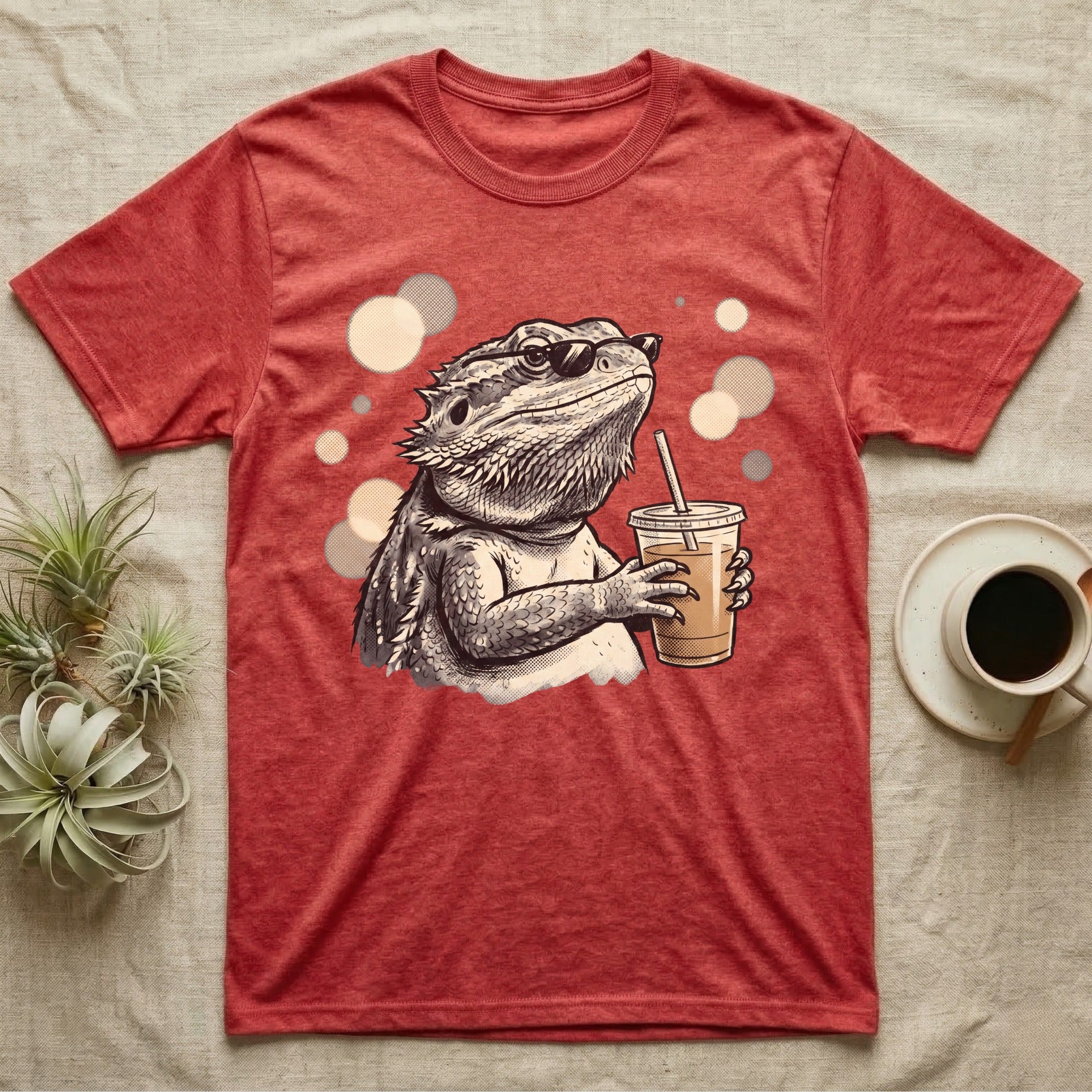 Cold Brew Bearded Dragon T-Shirt in Heather Red — Flat near-photoreal illustration of a bearded dragon in tiny sunglasses holding a cold brew with warm bokeh.