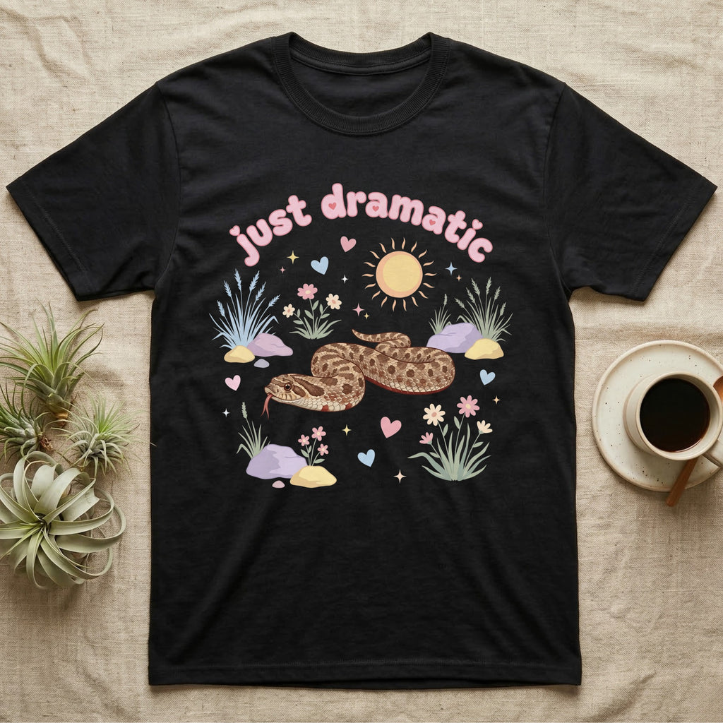 Western Hognose Snake Baby T-Shirt in Black — Pastel western hognose snake in a low coil with tongue out among grasses, puffy pink bubble wordmark "just dramatic" above.