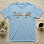 Amazon Milk Frog Branch T-Shirt in Light Blue — Four banded Amazon milk frogs perched along one slender branch, drawn in loose ink line and soft watercolour wash.