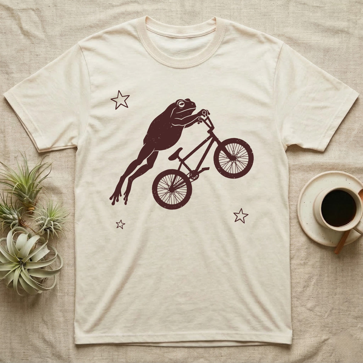 Tree Frog BMX T-Shirt in Natural — One-ink worn screen print of a White's tree frog riding a BMX bike mid-air, body stretched straight out behind the handlebars.
