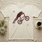 Tree Frog BMX T-Shirt in Natural — One-ink worn screen print of a White's tree frog riding a BMX bike mid-air, body stretched straight out behind the handlebars.