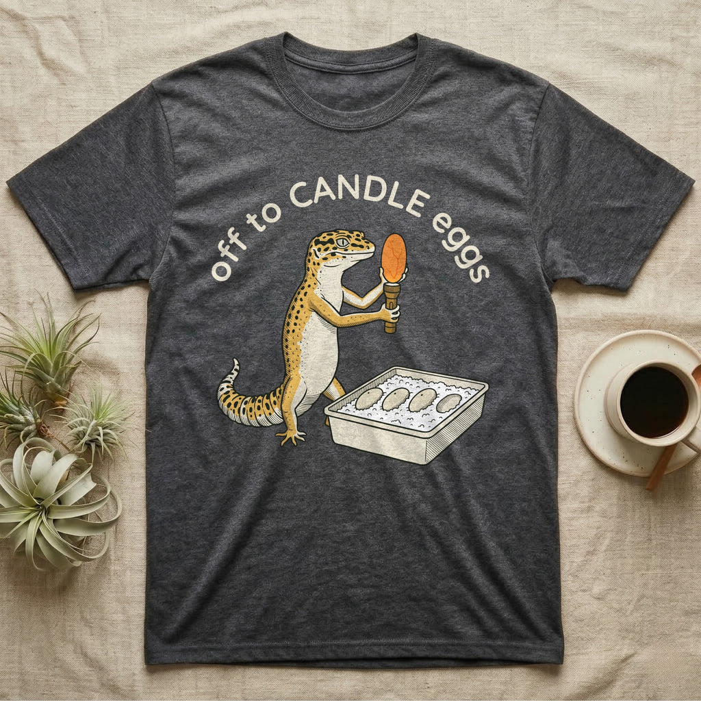 Leopard Gecko Candling T-Shirt in Dark Heather — Leopard gecko holding a torch under a glowing orange egg beside a tub of eggs, under the words off to CANDLE eggs