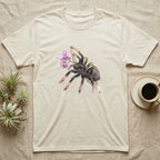 Pink-Toe Tarantula Blossom T-Shirt in Natural — Watercolor illustration of a charcoal pink-toe tarantula with salmon toe tips holding an orchid blossom sprig, on a dark grey t-shirt.