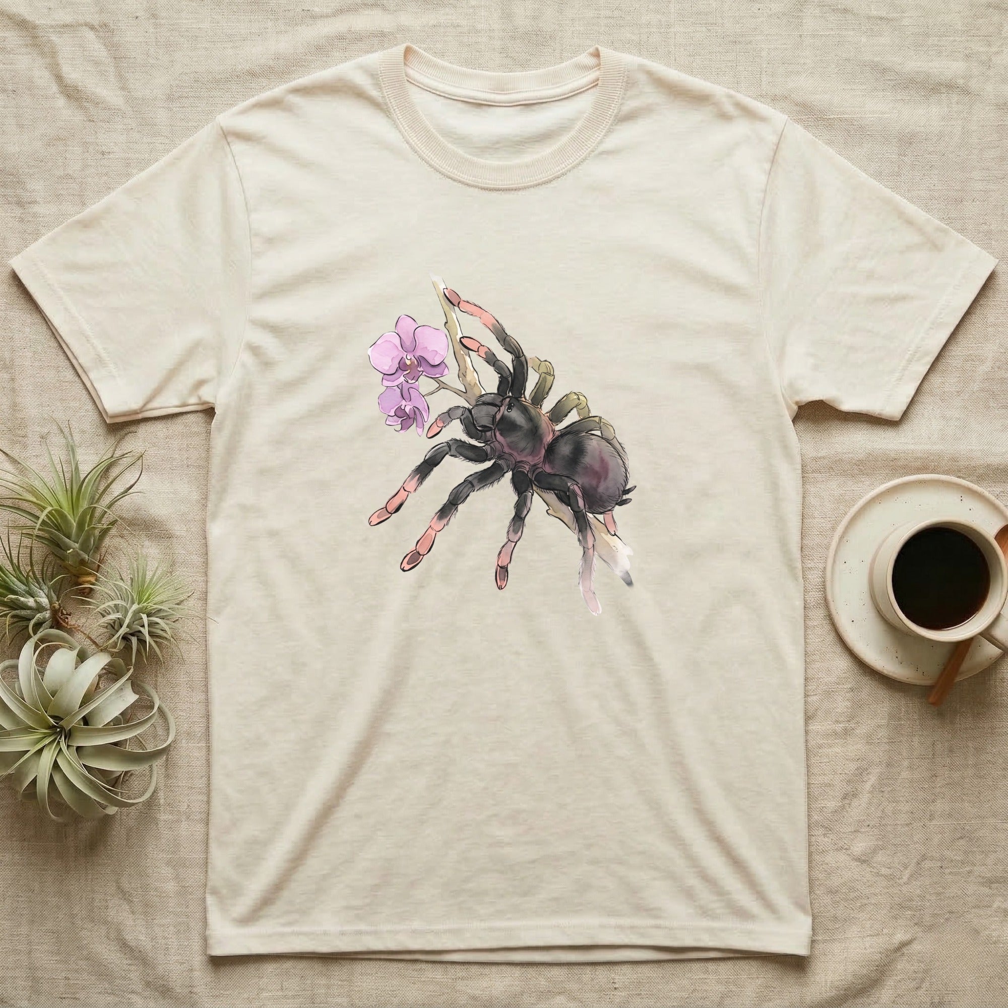Pink-Toe Tarantula Blossom T-Shirt in Natural — Watercolor illustration of a charcoal pink-toe tarantula with salmon toe tips holding an orchid blossom sprig, on a dark grey t-shirt.