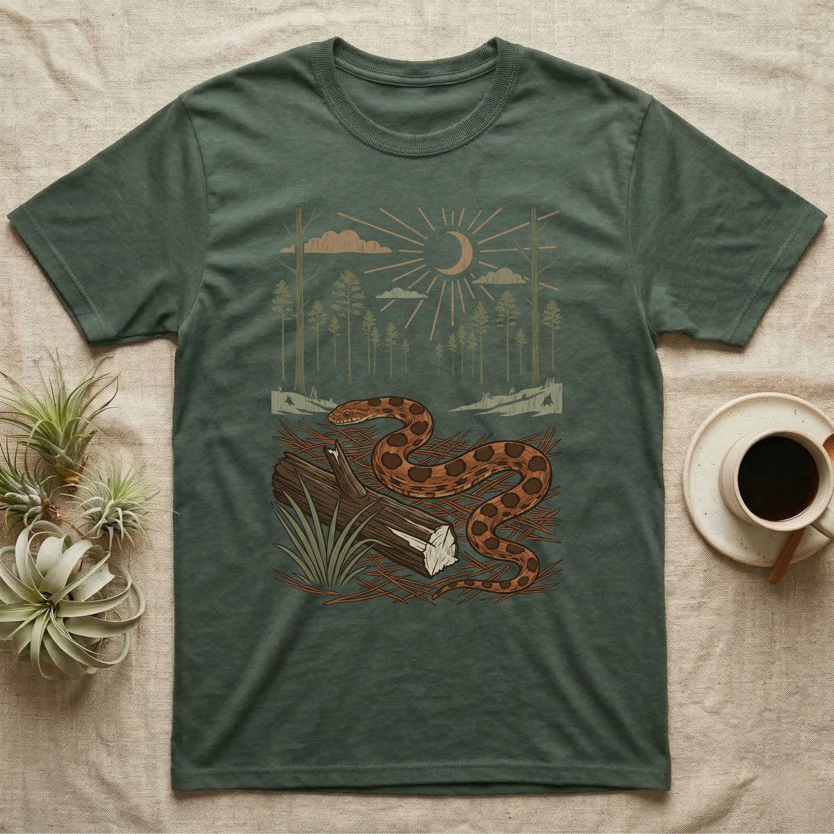 Corn Snake Home Range T-Shirt in Military Green — Woodcut-style illustration of a corn snake winding across pine straw beside a split log with pine trees behind, no on-shirt text.